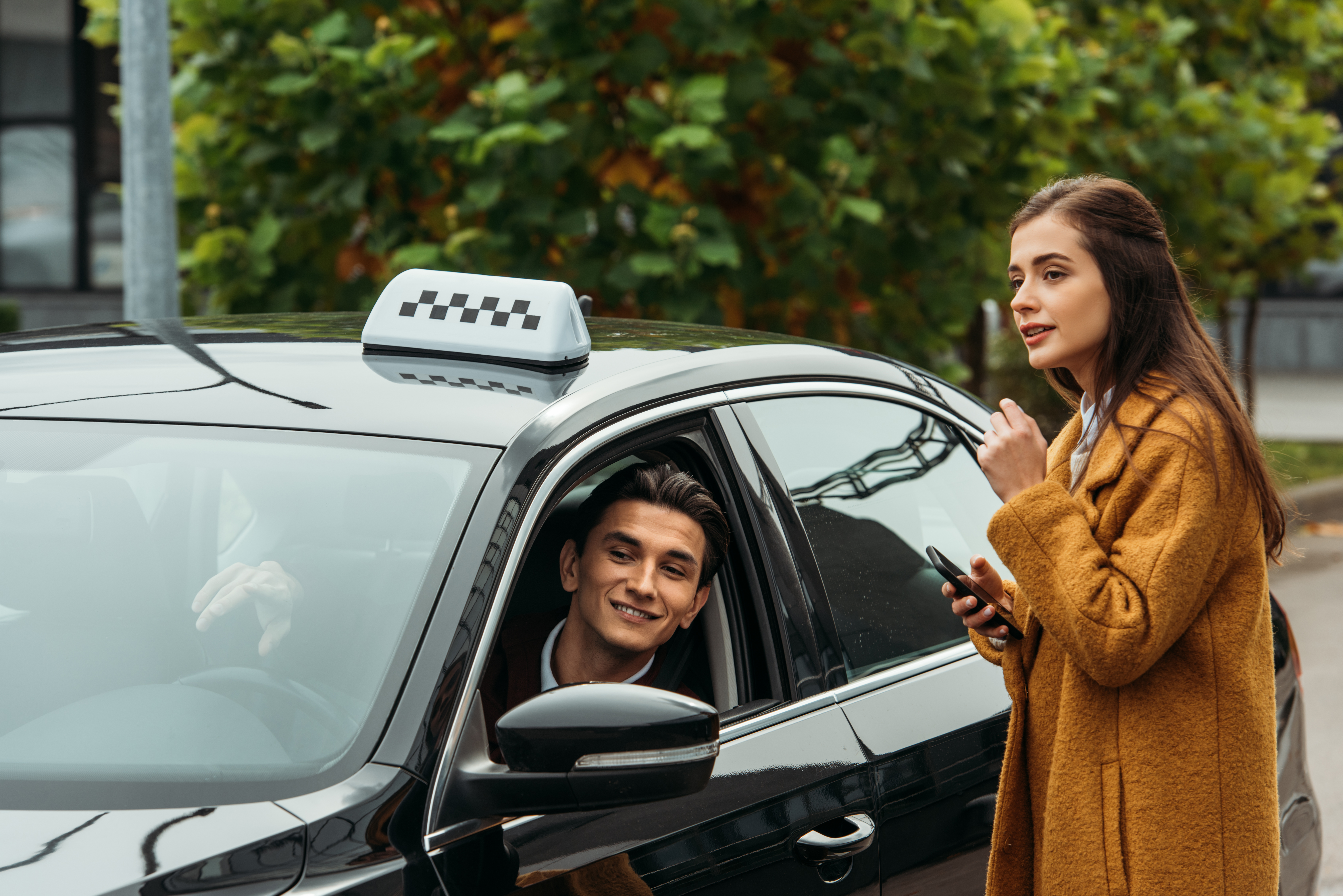 Young woman holding smartphone and talking to smiling taxi driver